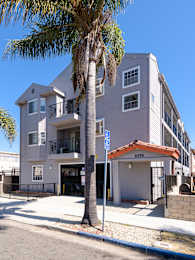 A palm tree stands in front of a two-story building with a garage.