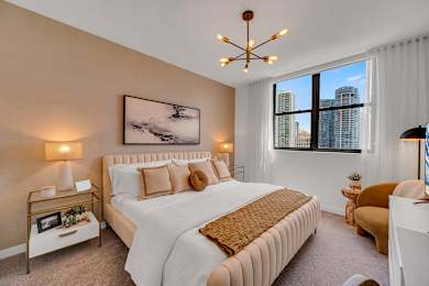 A bedroom with a large bed, a painting on the wall, and a window with a view of the city.