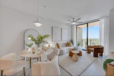 A modern living room with a dining table set for two and a view of the balcony.