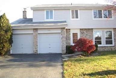 A house with a white garage door and a red bush.