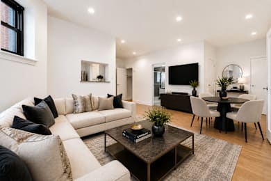 A modern living room with a white sofa, a black coffee table, and a TV mounted on the wall.