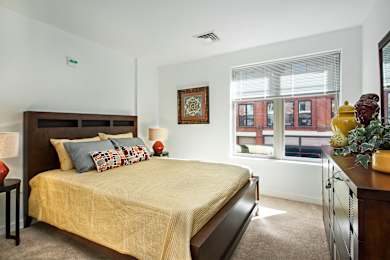 A bedroom with a bed, nightstand, and a window with blinds.