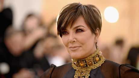 A woman with short hair and a black outfit is wearing a large, ornate necklace.