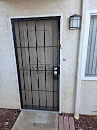 A black metal gate with a decorative design is on a white wall.