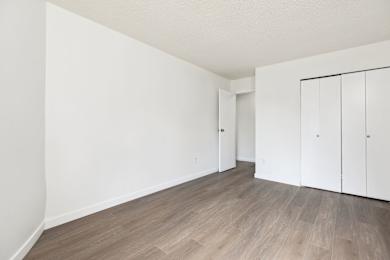 A room with white walls and wooden flooring with two white cupboards.