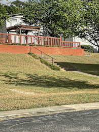 A red brick wall with a metal railing and steps leading up to a house.