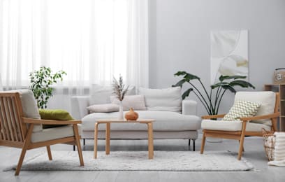 A living room with a white couch, a wooden chair, a wooden table, and a potted plant.
