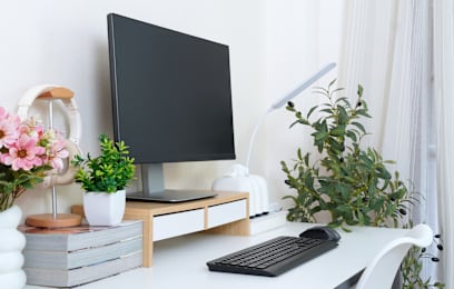 A black monitor sits on a desk with a keyboard and a plant.