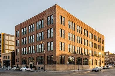 A large red brick building with many windows and cars parked in front.
