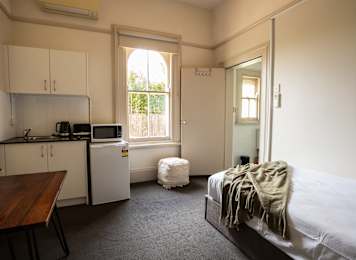 A bedroom with a bed covered in a blanket and a kitchen area with a microwave and oven.