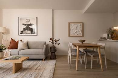 A living room with a grey sofa, a wooden table with four chairs, and two framed pictures on the wall.