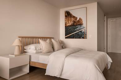 A bedroom with a large bed and a picture of a cliff by the sea on the wall.
