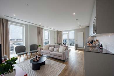 A modern living room with a grey sofa, a coffee table, and a kitchen area in the background.