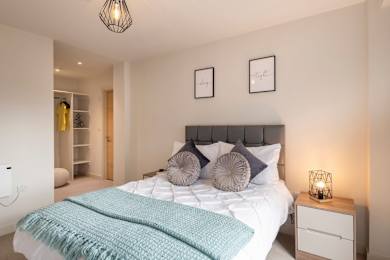 A bedroom with a large bed and a nightstand with a lamp at The Trilogy Apartments, Manchester