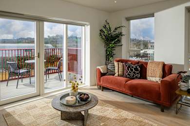 A living room with a red couch and a glass door leading to a balcony.
