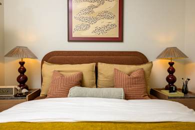 A bed with a white comforter and a yellow blanket is flanked by two lamps on either side.