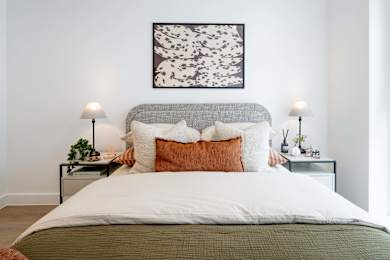 A bed with a grey headboard and two orange pillows is in the image.