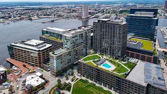 A large building with a green roof is surrounded by other buildings and a body of water.