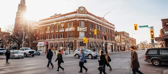 People crossing a street in a city with a large building in the background.