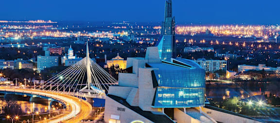 A cityscape at night with a prominent building featuring a spire and a modern design.