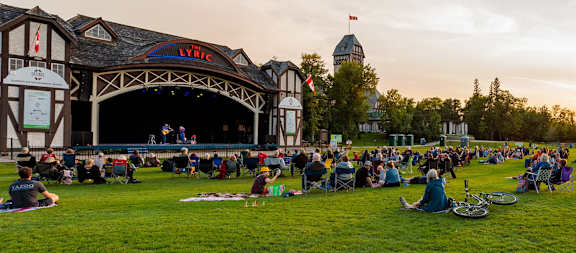 A large crowd of people are sitting on the grass in front of a stage with a sign that says "LYRIC".