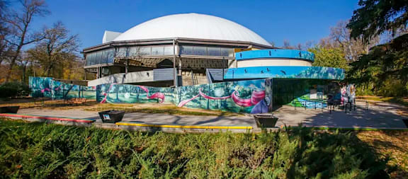 A large white dome structure with a blue and green mural on the wall in front of it.