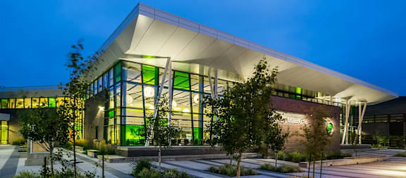 A modern building with a white roof and glass windows is illuminated at night.