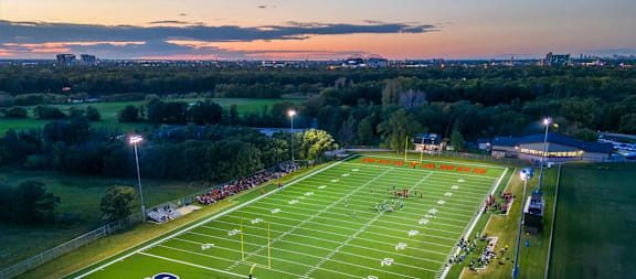 A football field is illuminated with orange lights at dusk.