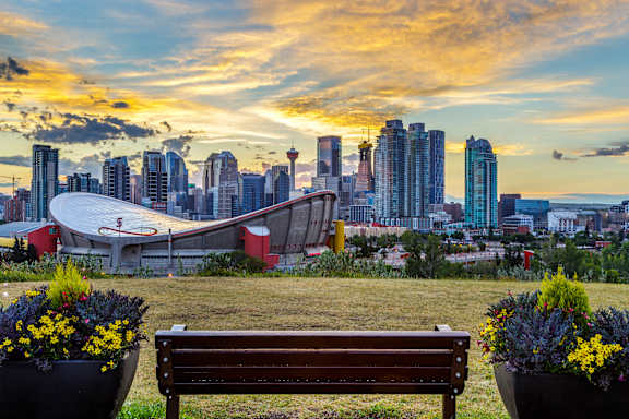 A bench is in the foreground of a city skyline at sunset.