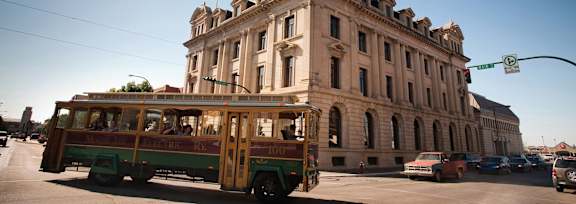 A green and yellow trolley car is on a street in front of a large building.