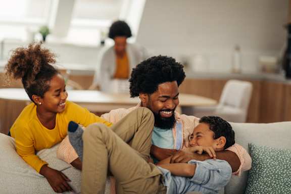 A family of three is sitting on a couch in a living room.