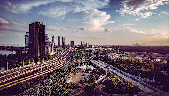 A cityscape with a highway and buildings under a blue sky with clouds.