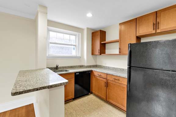 Floor Plan  A kitchen with a black refrigerator, wooden cabinets, and a marble countertop.