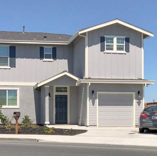 A modern house with a grey and white exterior and a grey car parked in front.