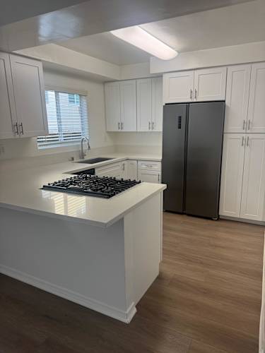 Floor Plan  A kitchen with wood flooring, white cabinets and a black fridge.