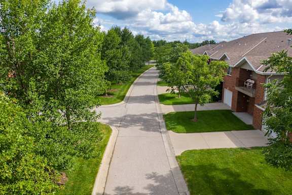 A tree-lined street with a large apartment building with driveways to the right