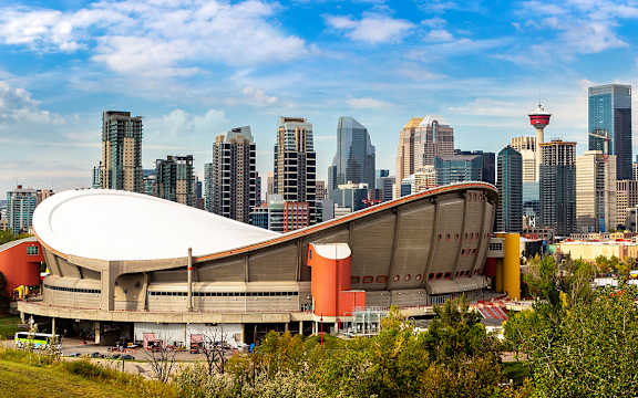 A large stadium with a unique design is in the foreground with a city skyline in the background.