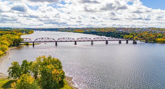 A bridge spans a river with trees on the left and a cloudy sky above.