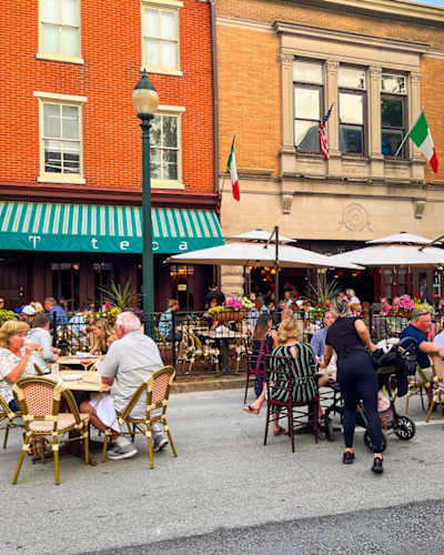 A group of people are sitting at outdoor tables under umbrellas.