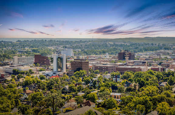 A cityscape with buildings and trees under a blue sky with clouds.