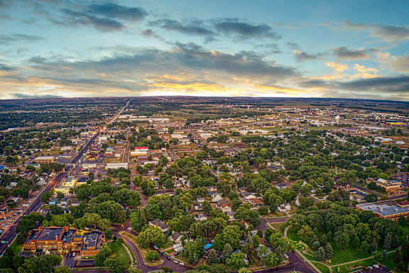 A cityscape with roads, buildings, and greenery under a cloudy sky.