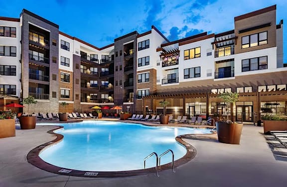 A large swimming pool is surrounded by a patio area with lounge chairs and potted plants.
