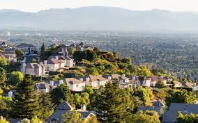 A cityscape with houses and trees in the foreground and a hazy mountain range in the background.