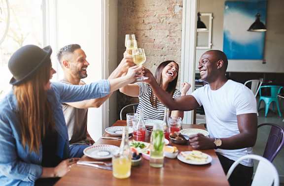 a group of people sitting around a table laughing and drinking wine