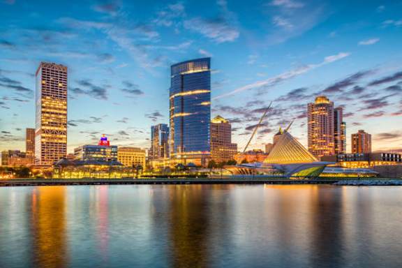 A city skyline at dusk with buildings reflecting in the water.