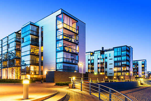 A modern building with glass windows and balconies is illuminated at dusk.
