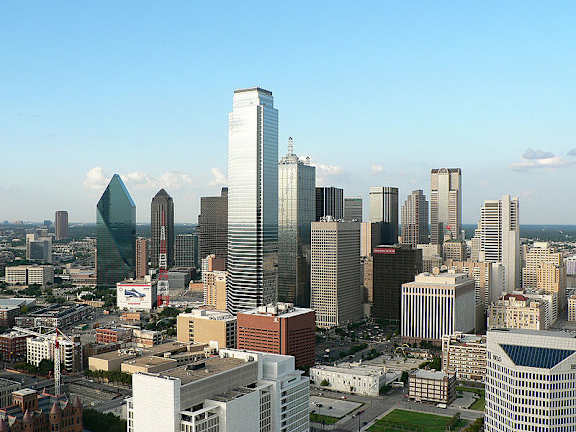 A cityscape with a variety of buildings, including a tall skyscraper with a pointed top.