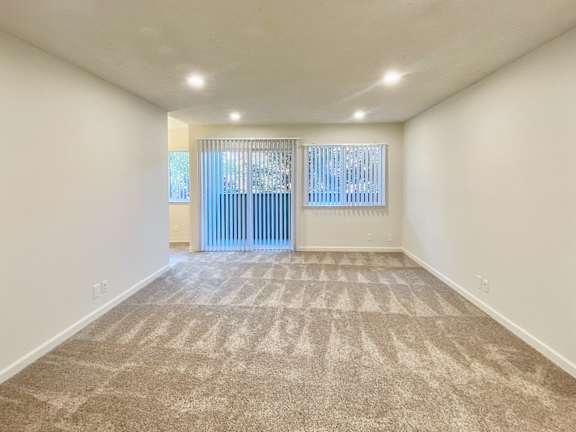 A room with a carpeted floor and a window with blinds.