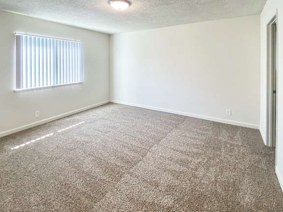 A room with a carpeted floor and a window with blinds.