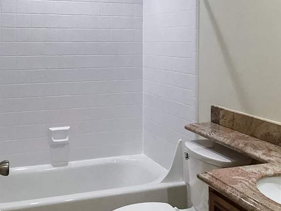 A white bathtub sits next to a toilet in a bathroom.